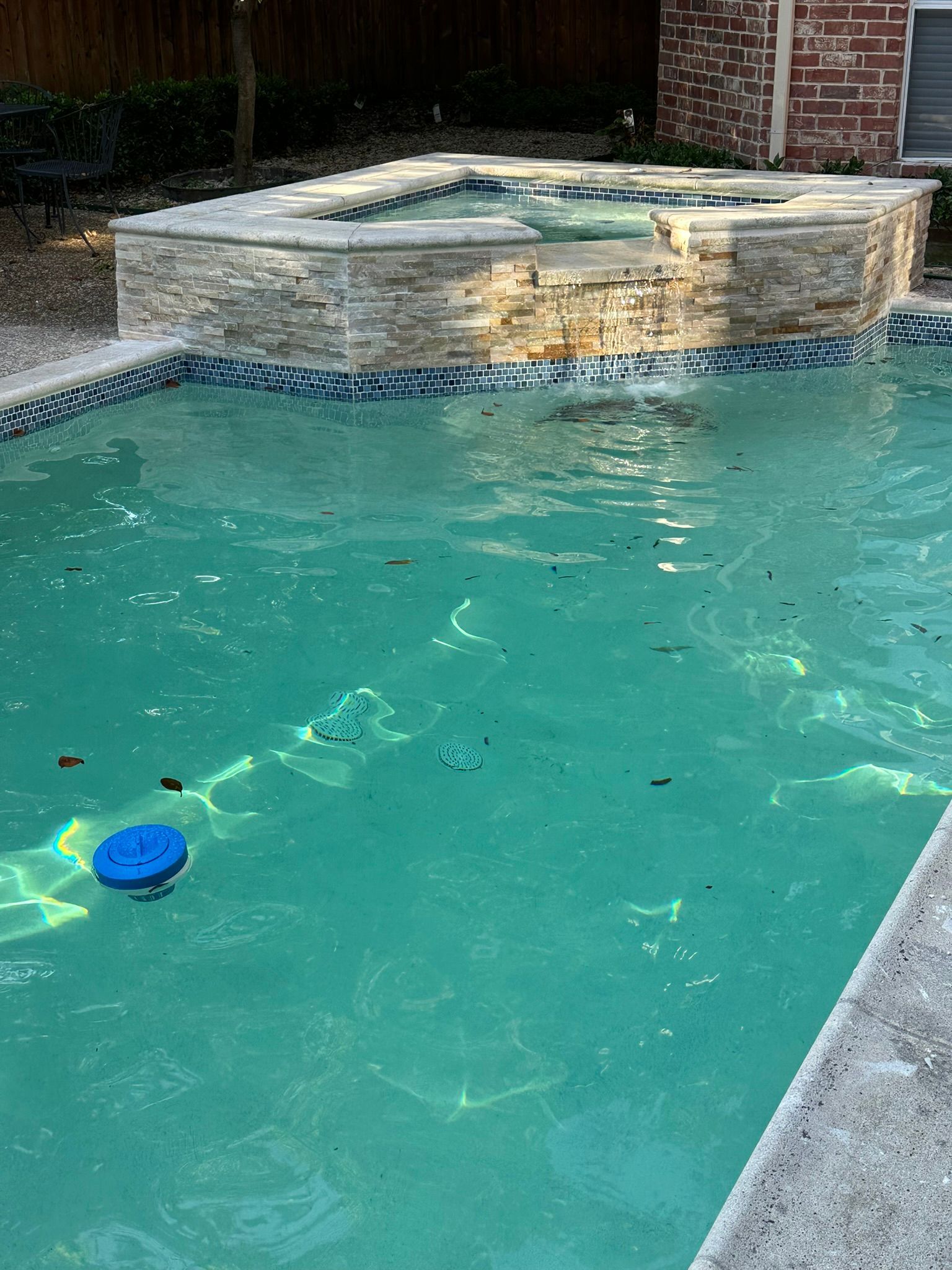 Pool with spa, turquoise water, stone facing, blue tile trim, and blue float.
