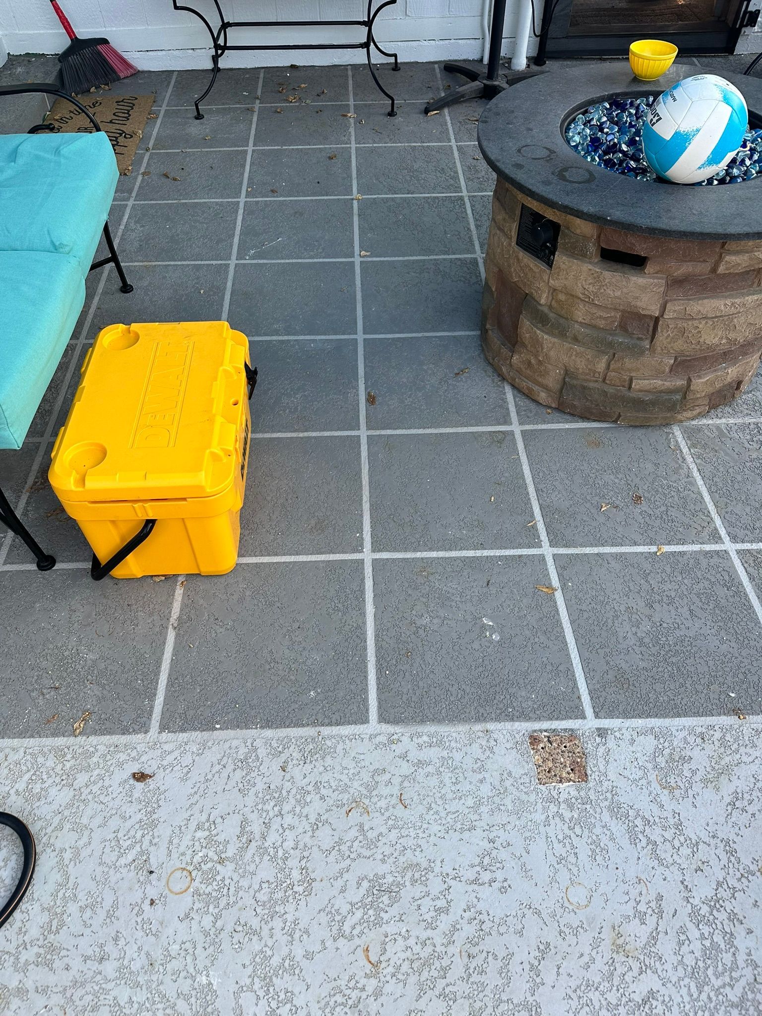 Yellow cooler on a gray patio, next to a teal bench and a fire pit with a blue and white ball.