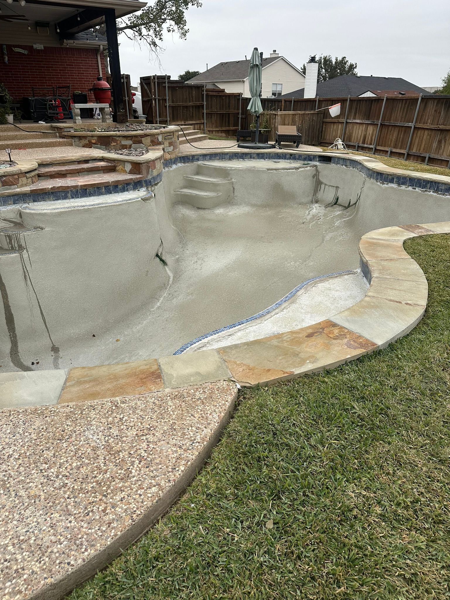 Empty swimming pool under construction, surrounded by stone and grass.