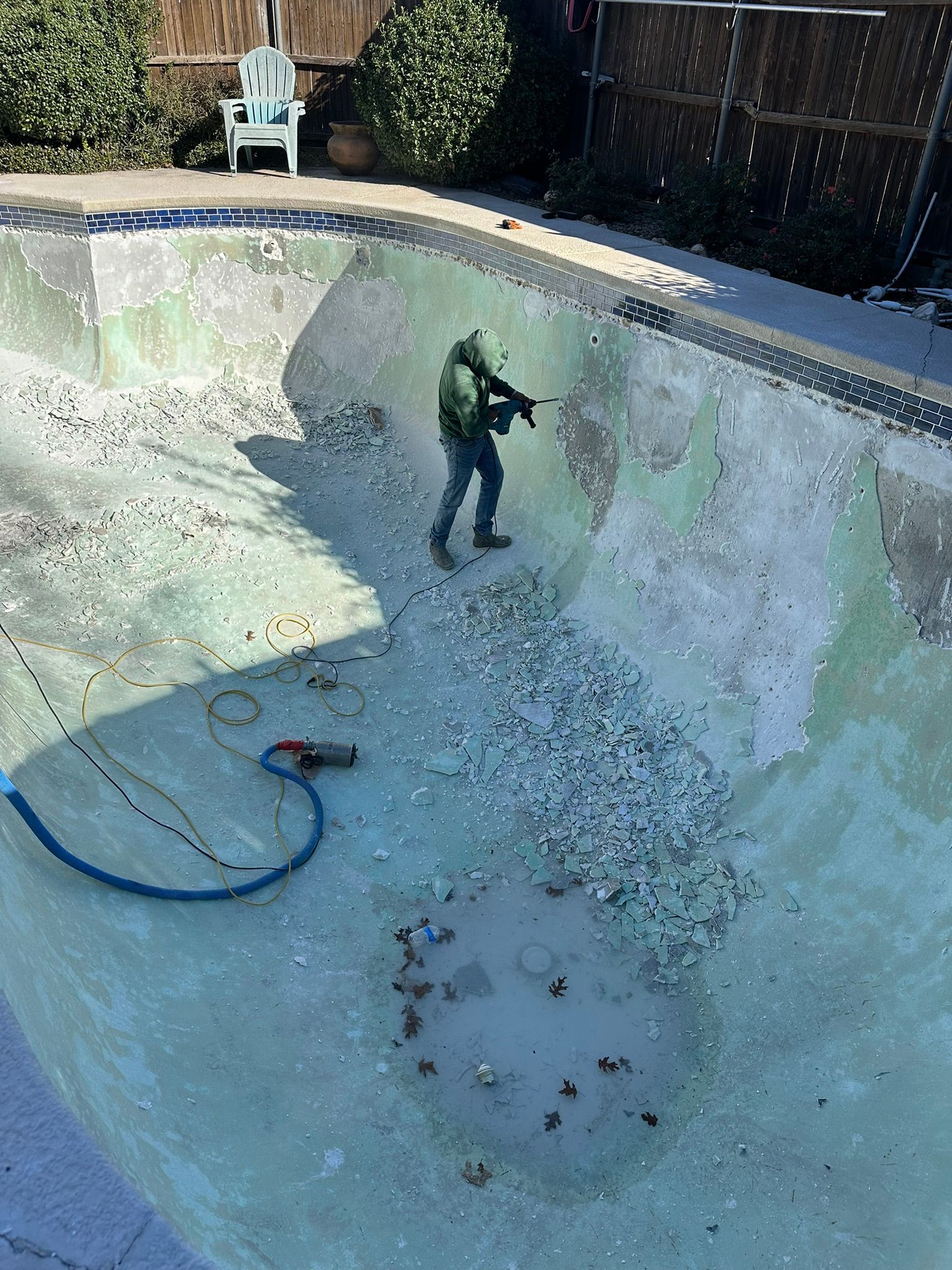 Person using a tool to clean a drained pool. Green and gray debris covers the pool floor.