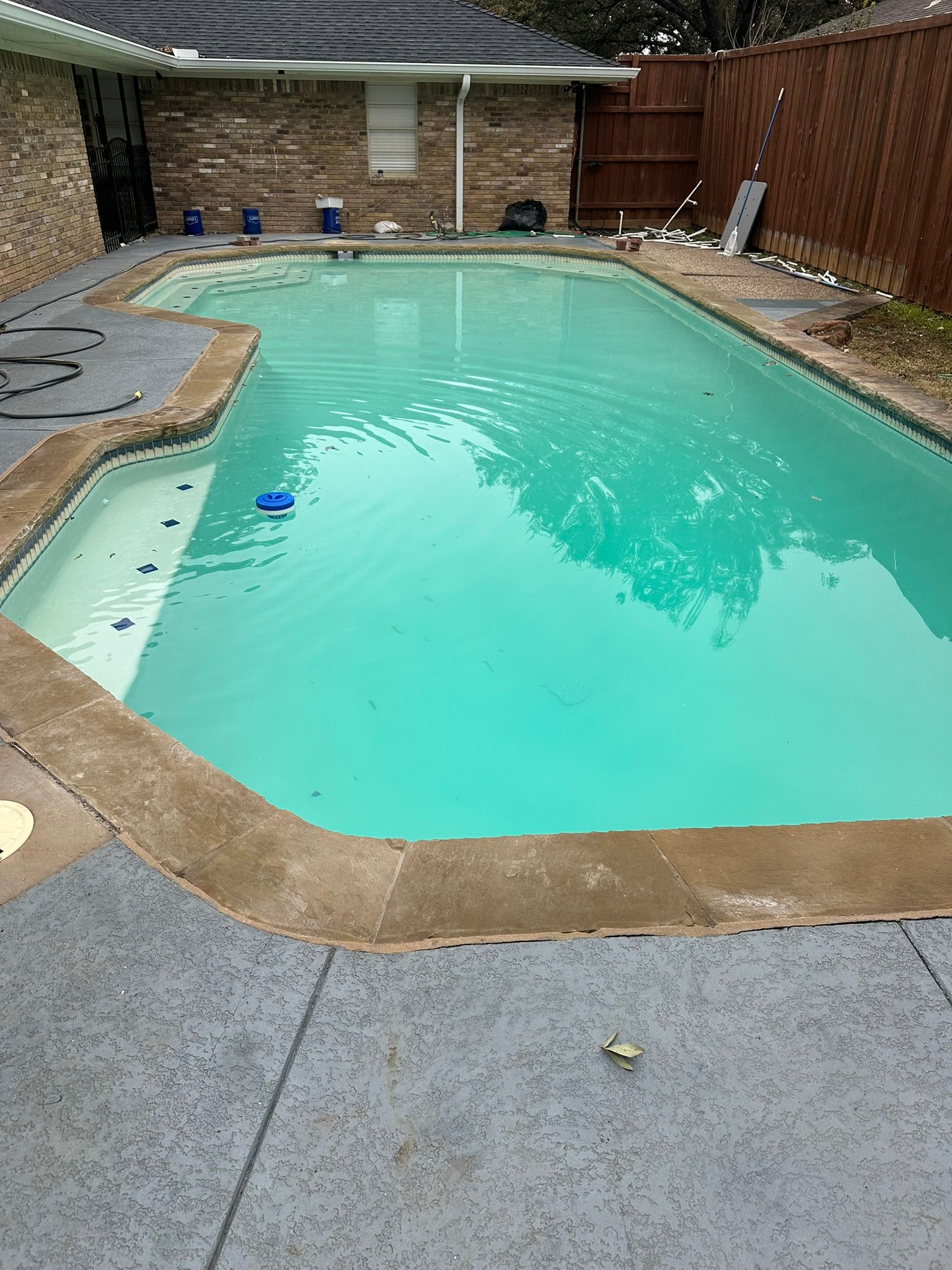Pool with turquoise water surrounded by concrete and a brown brick house.