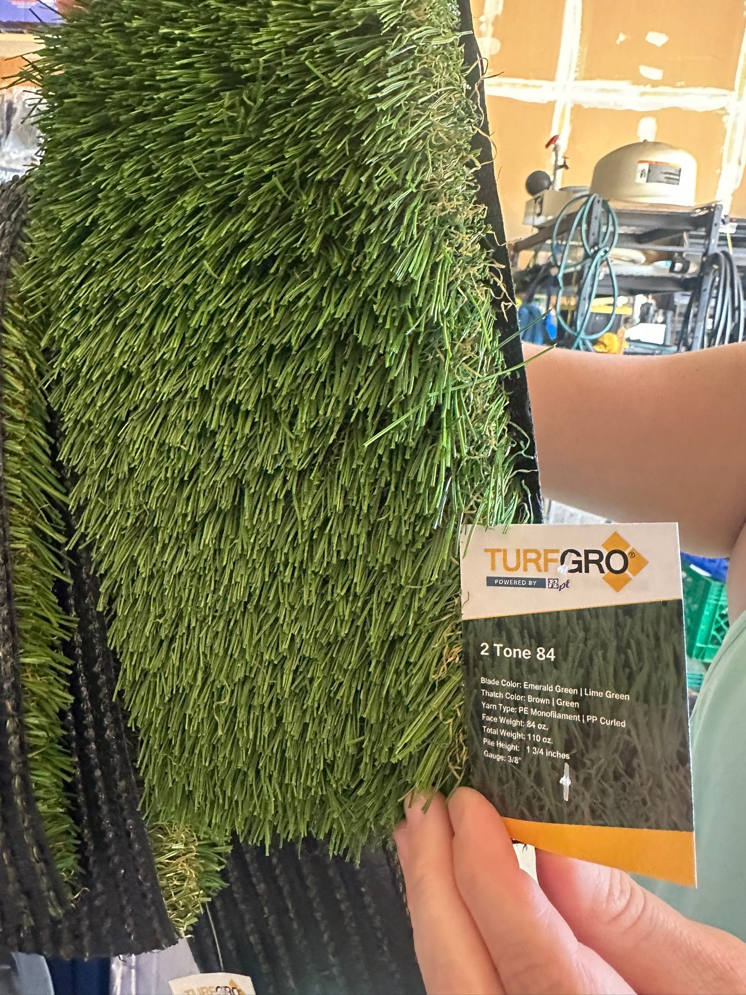 A person holds a sample of artificial turf labeled 