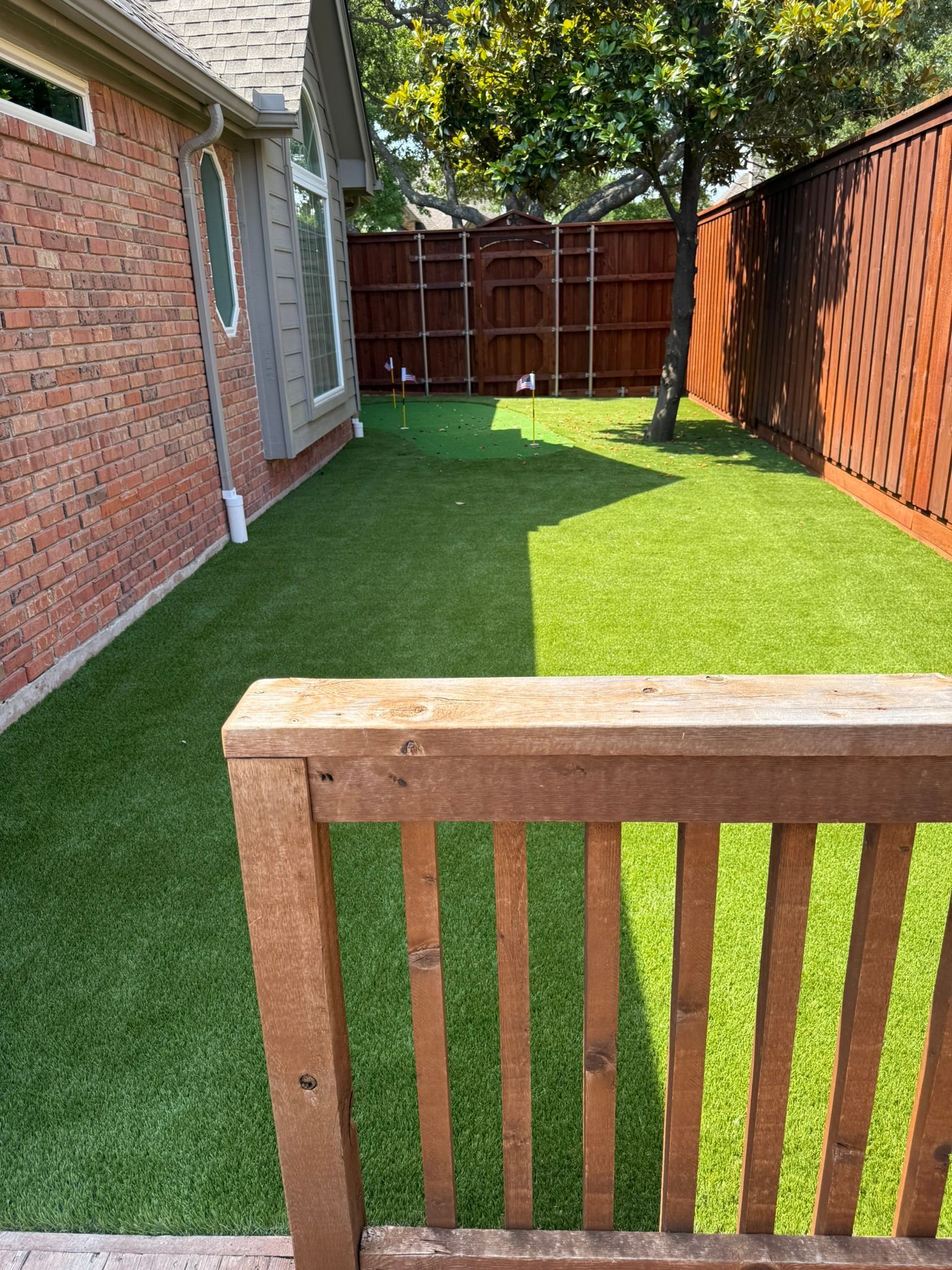 View of a backyard with artificial turf, brown fences, and a wooden railing.