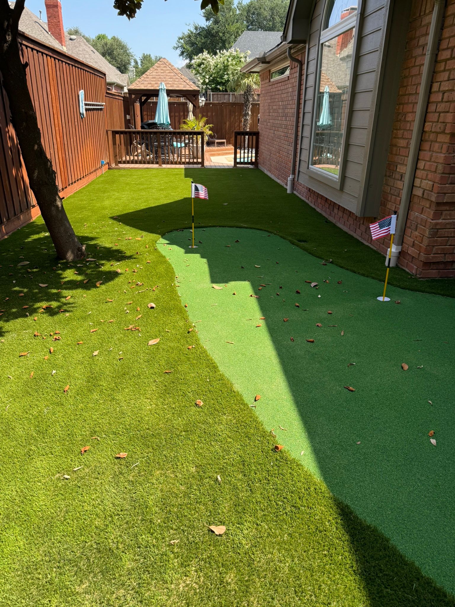 Backyard with a putting green, two flags, and a gazebo in the distance; sunny day.