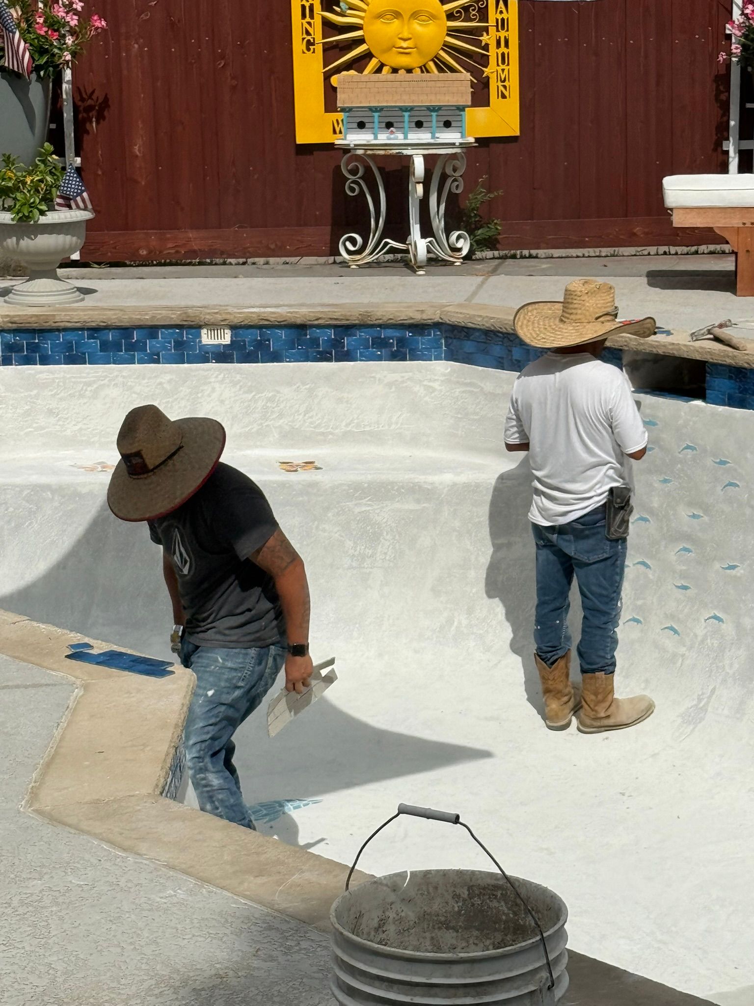 Two workers in hats resurfacing a swimming pool.