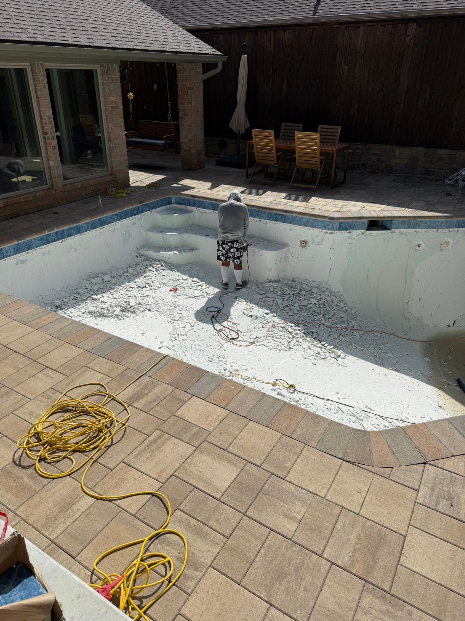 Person standing in a drained swimming pool filled with white pebbles; a brick patio surrounds it.
