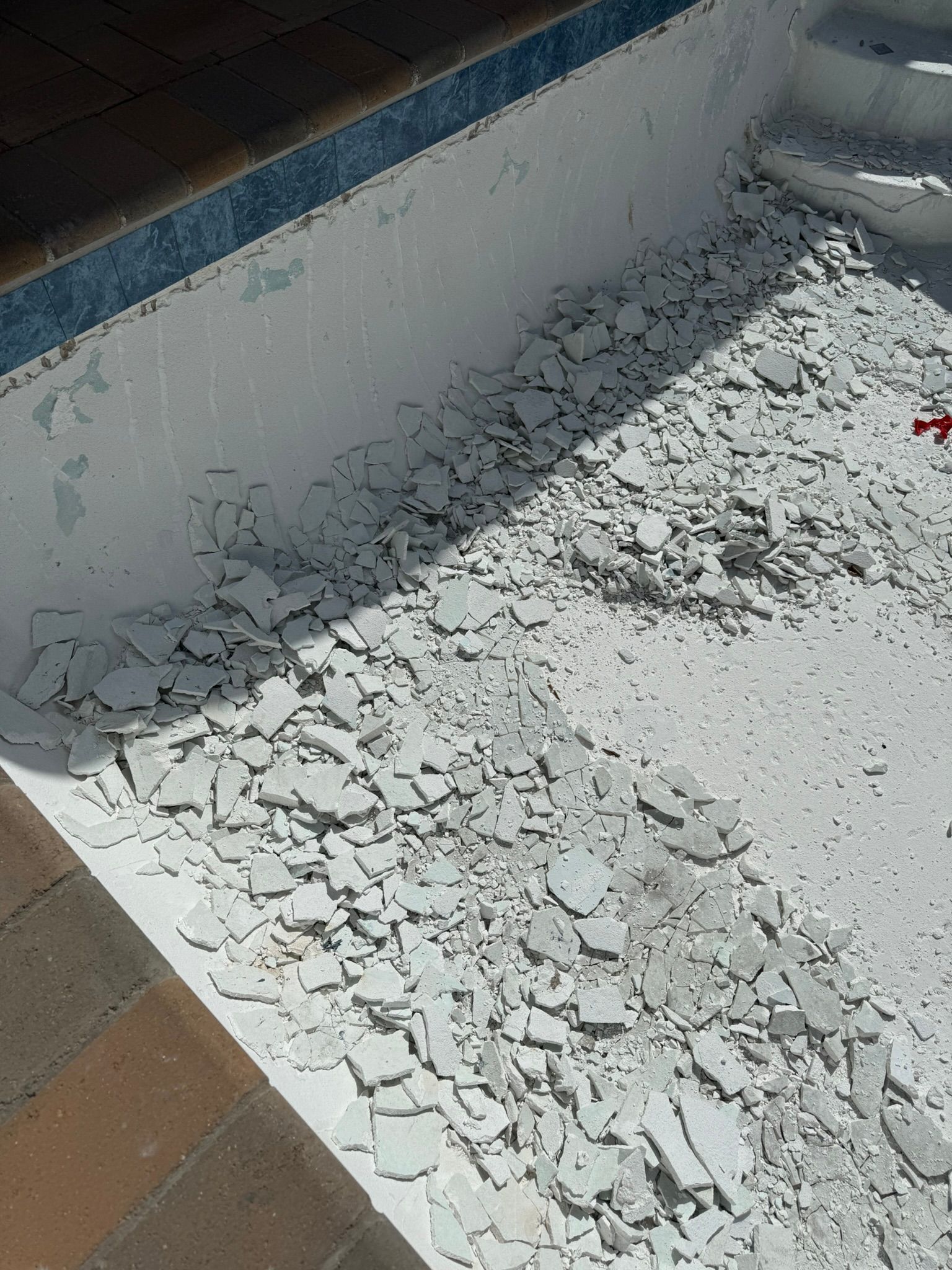 Pool interior with broken white tiles and debris along the steps.