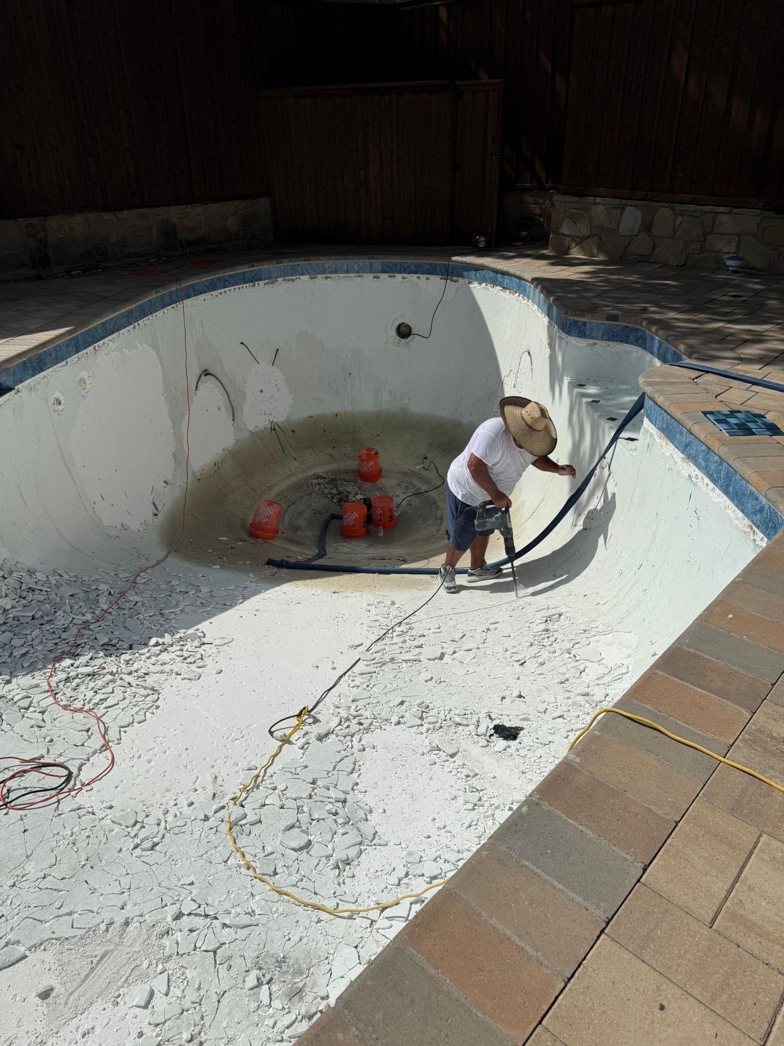 Person cleaning an empty, tiled swimming pool with a brush under bright sunlight.