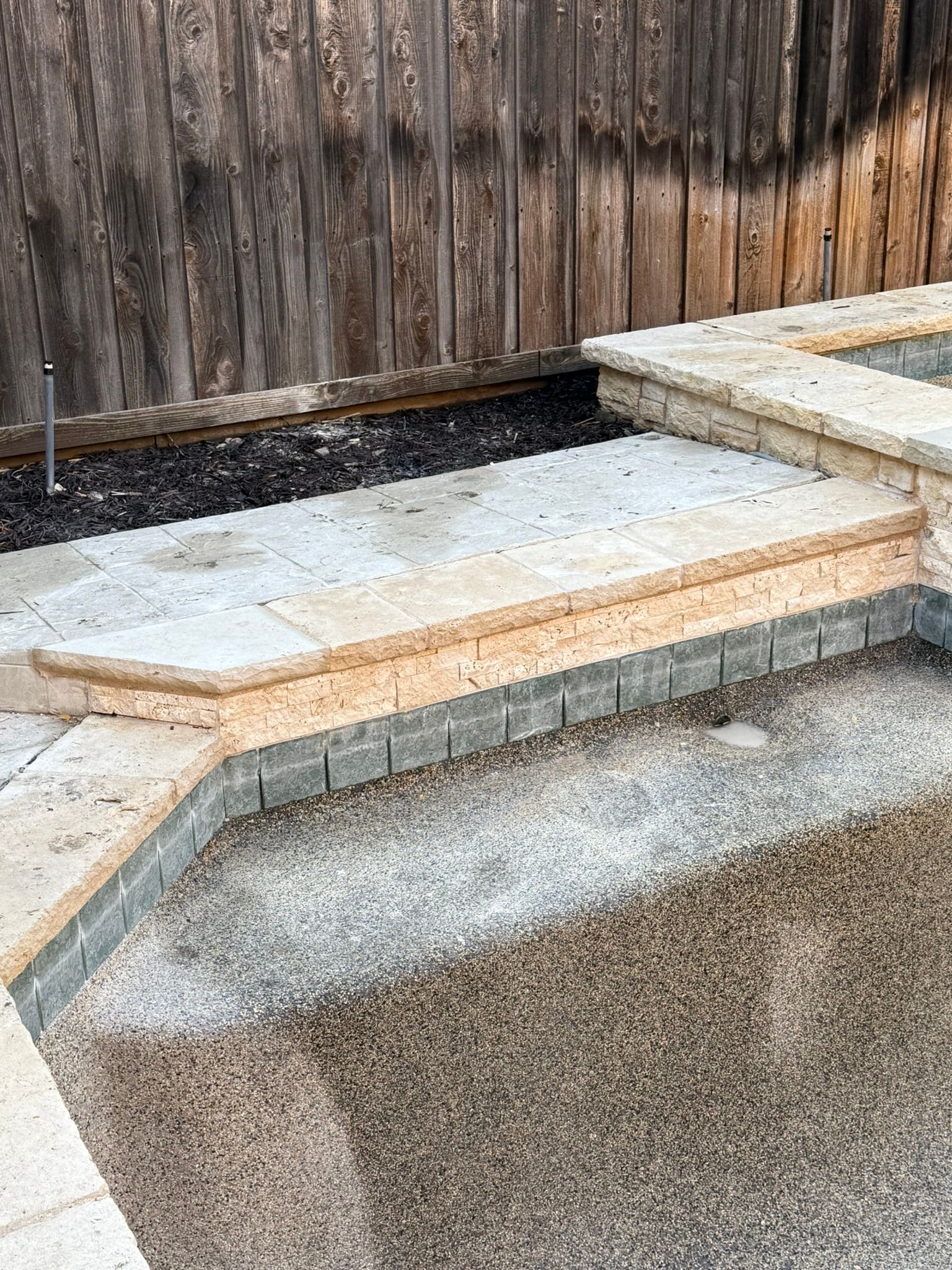 Stone pool with steps against a wooden fence.