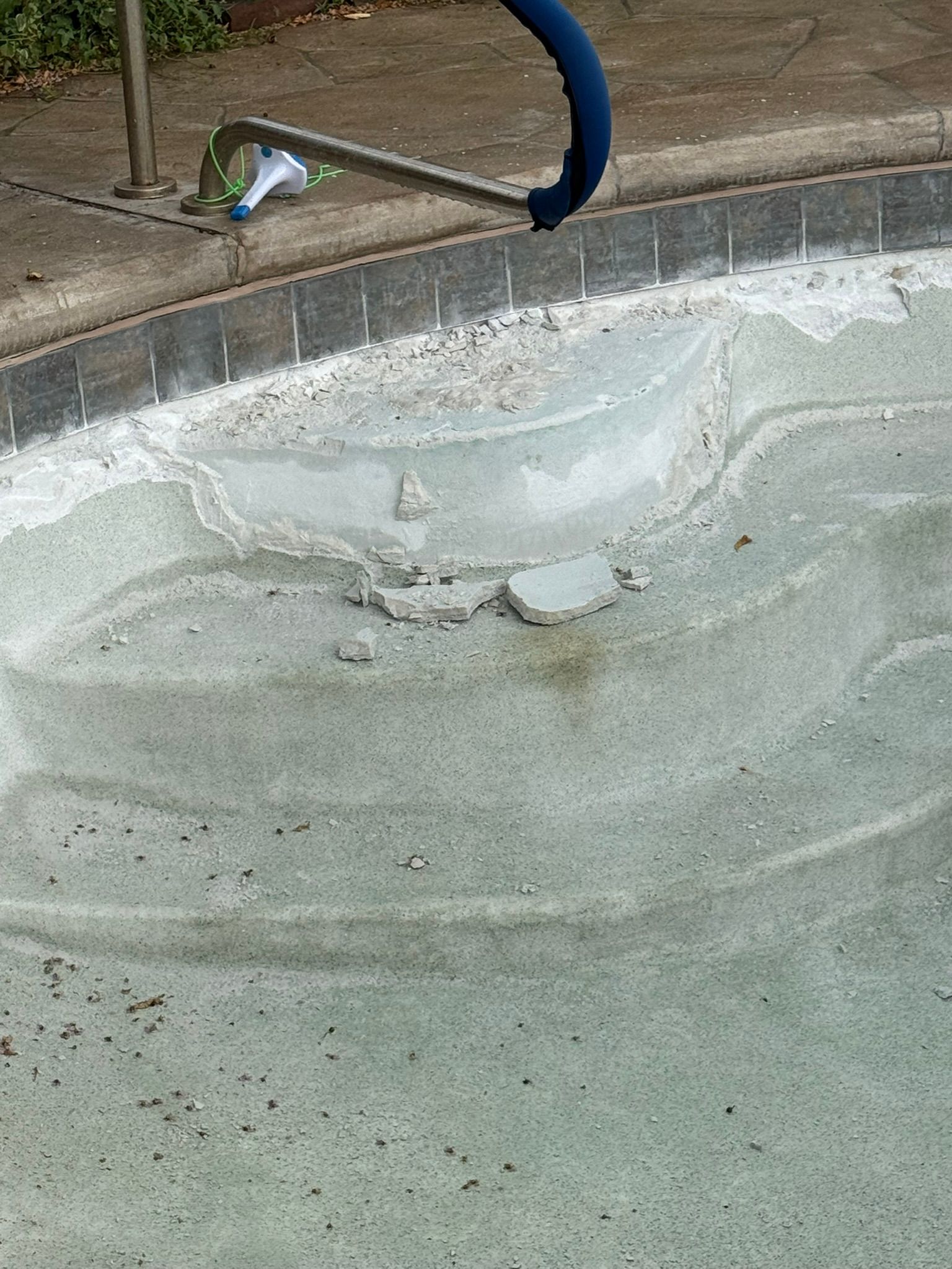 Pool steps with cracked surface, debris, and a blue hose along the edge.