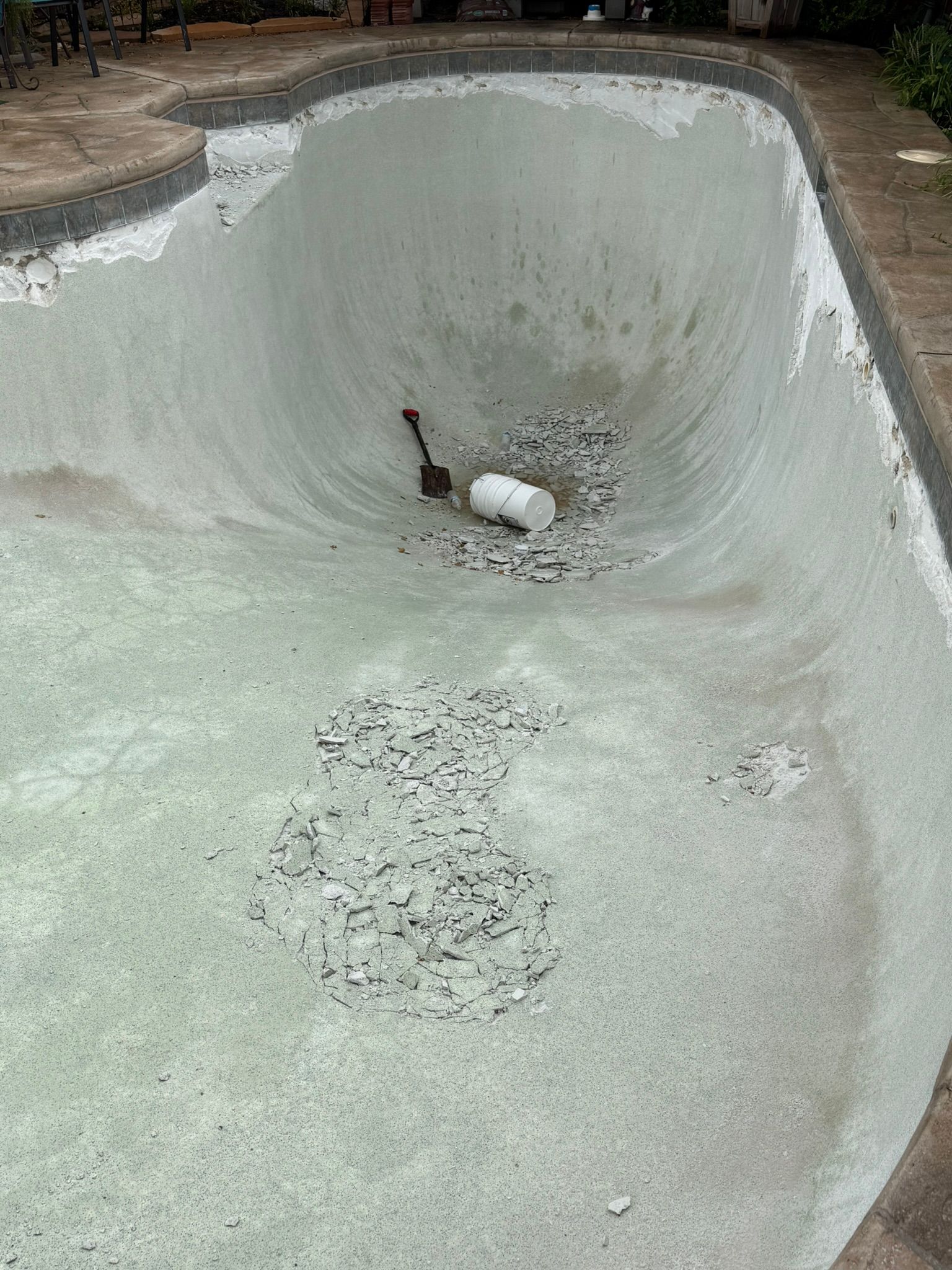 Empty swimming pool with grey plaster and debris inside.