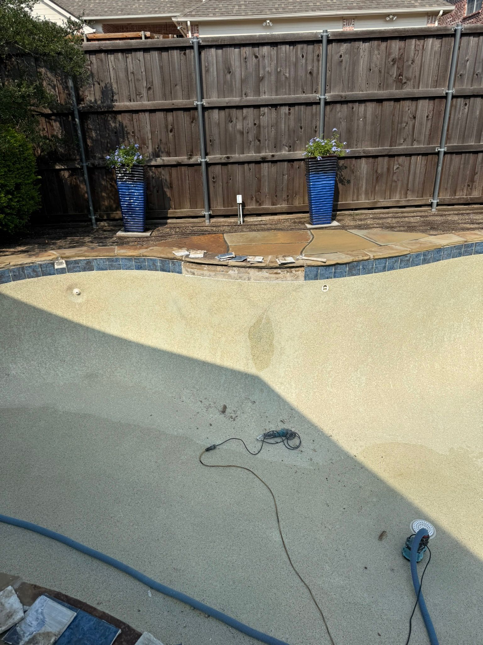 Empty pool with blue planters against a wooden fence. The pool's surface has a speckled appearance.