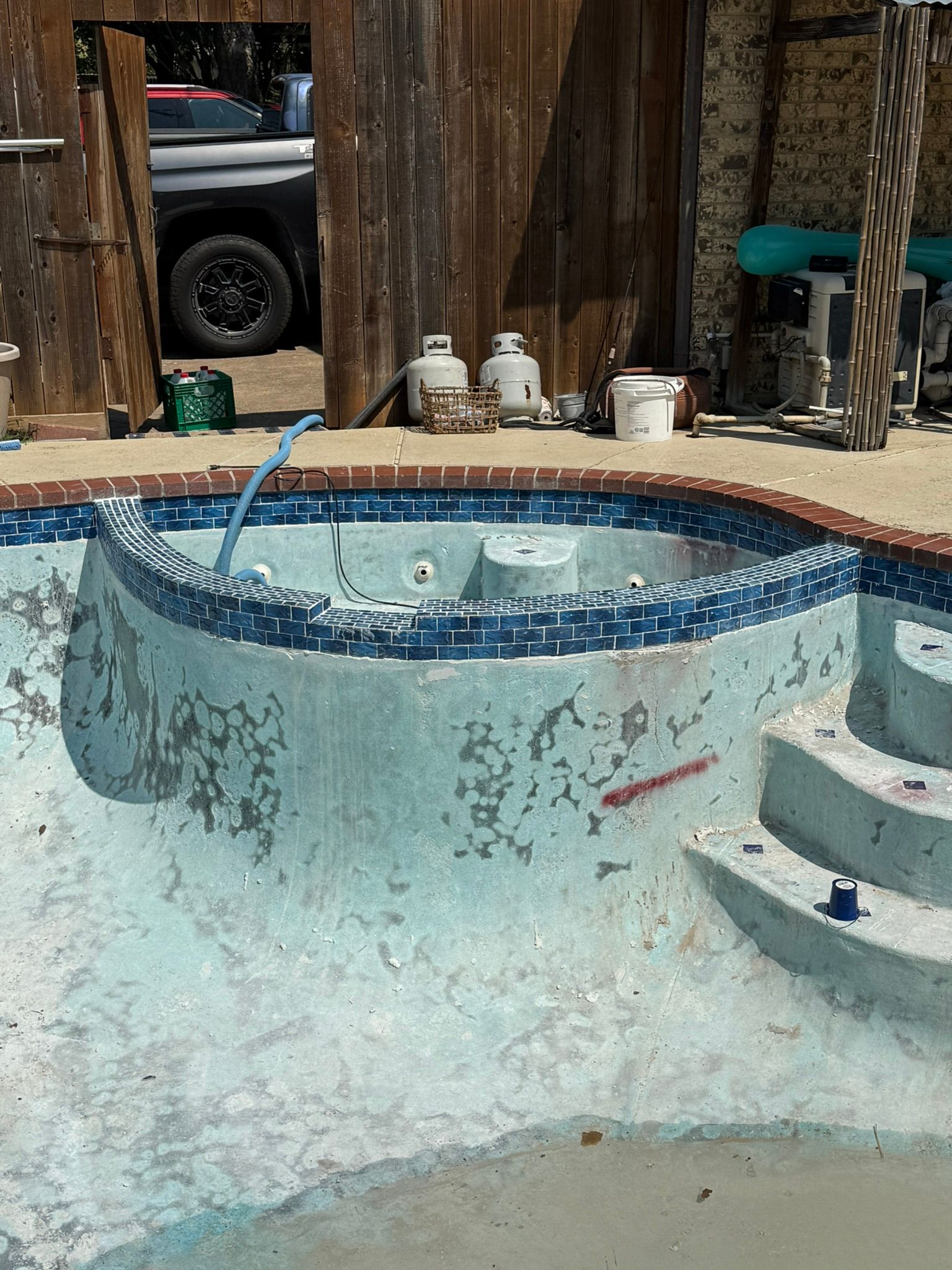 Empty pool with peeling blue plaster and surrounding equipment, steps, and brick coping.