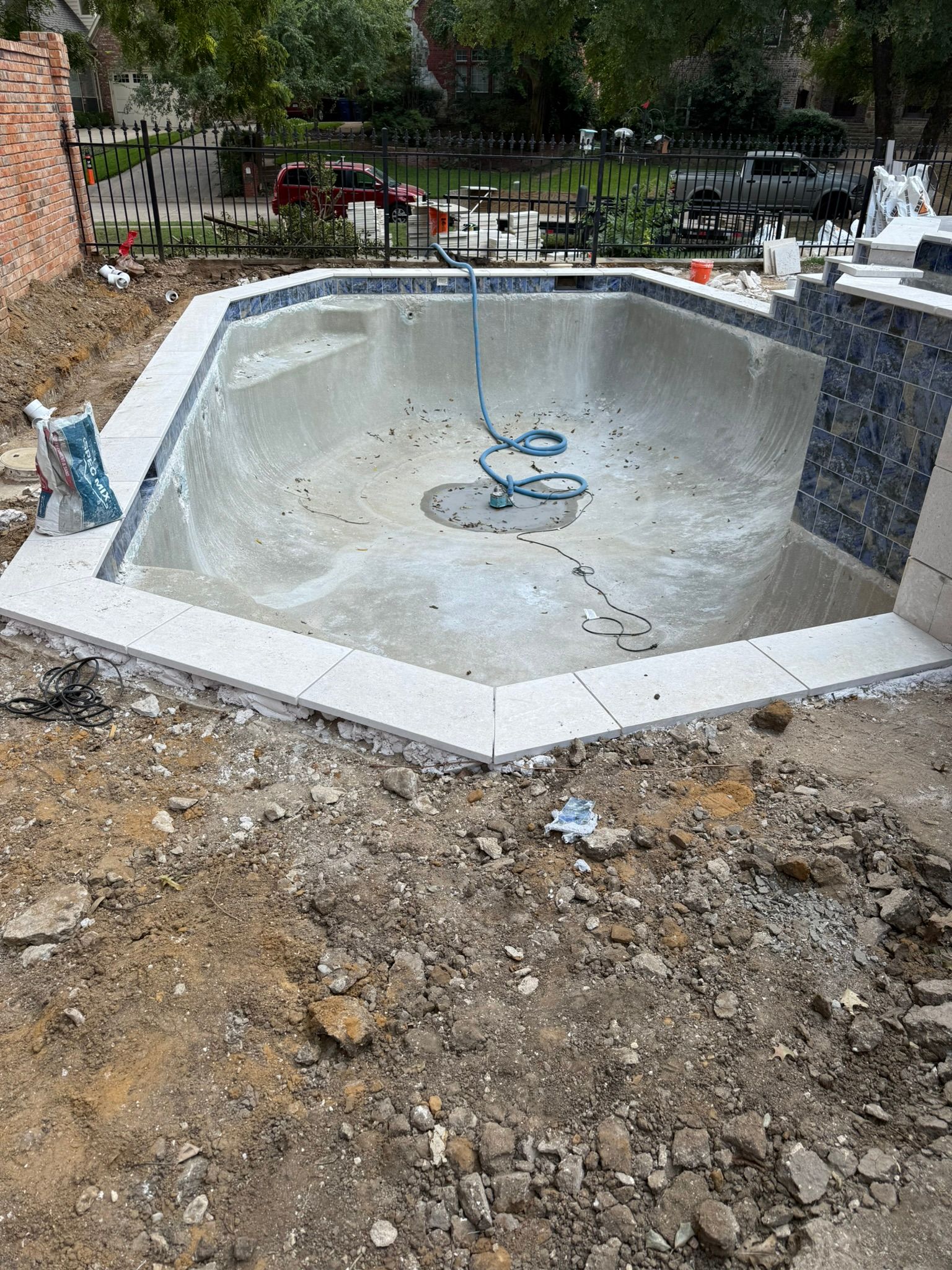 Partially built swimming pool with concrete basin and tiled coping. Construction materials and surrounding dirt.