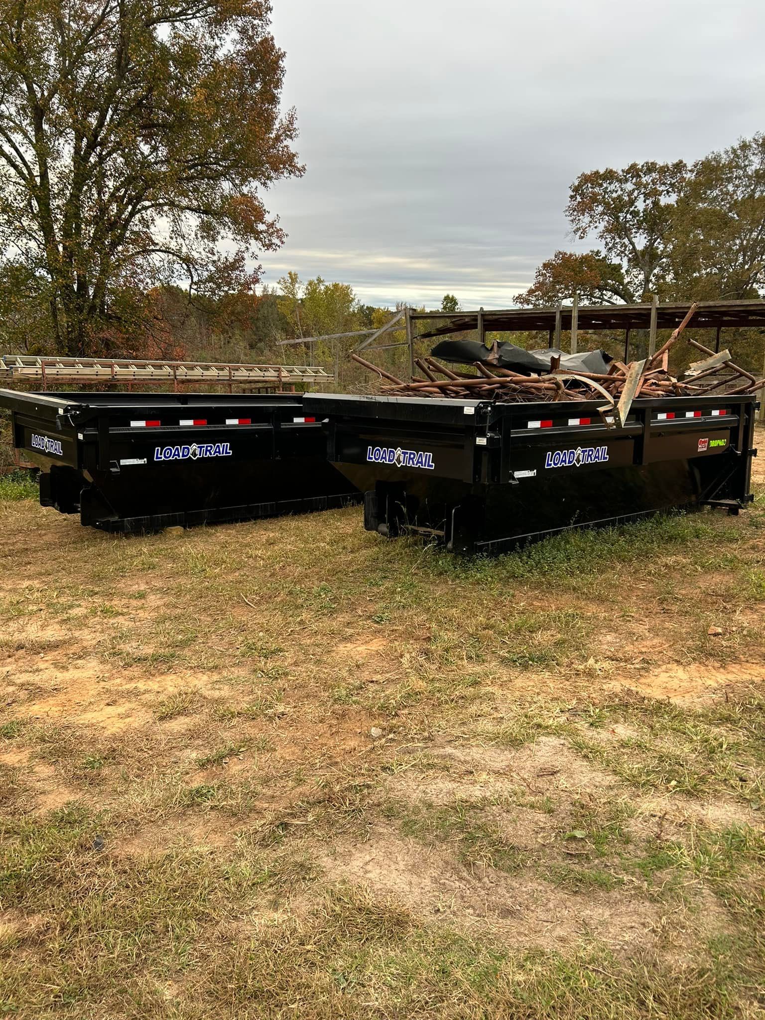 Two dumpsters are sitting on top of a grassy field.