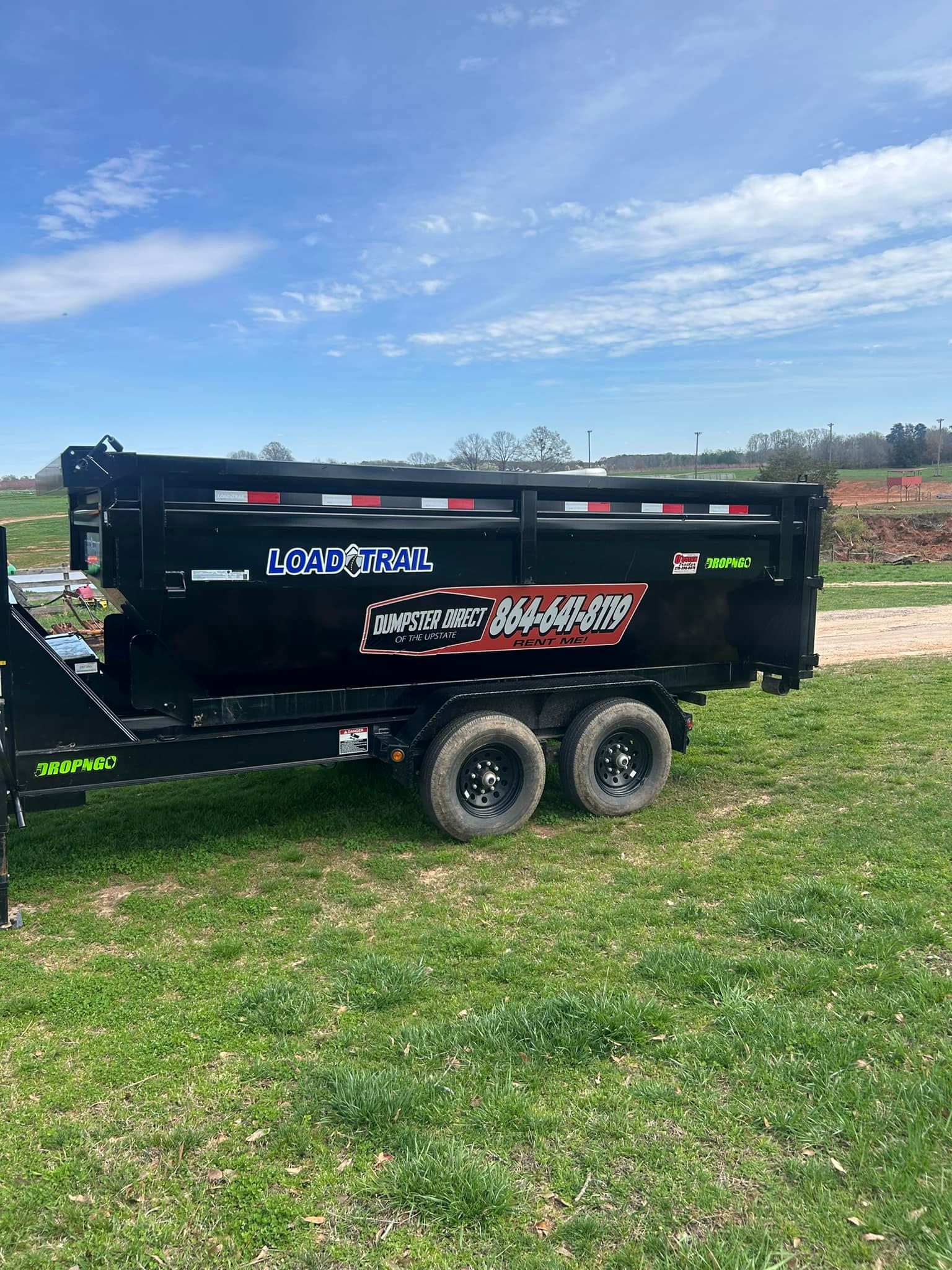 A dumpster trailer is parked in a grassy field.