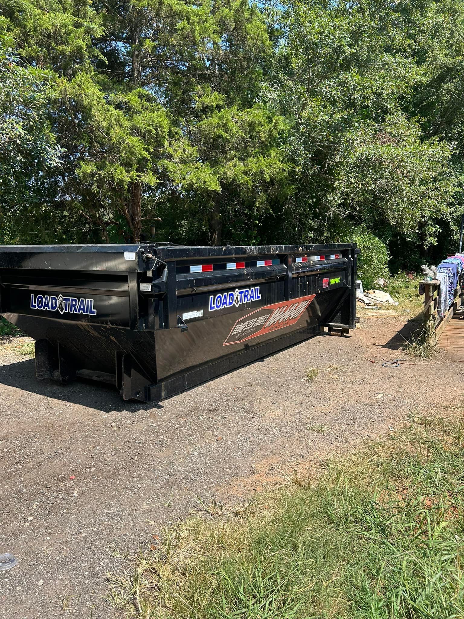 A dumpster is parked on the side of the road next to trees.