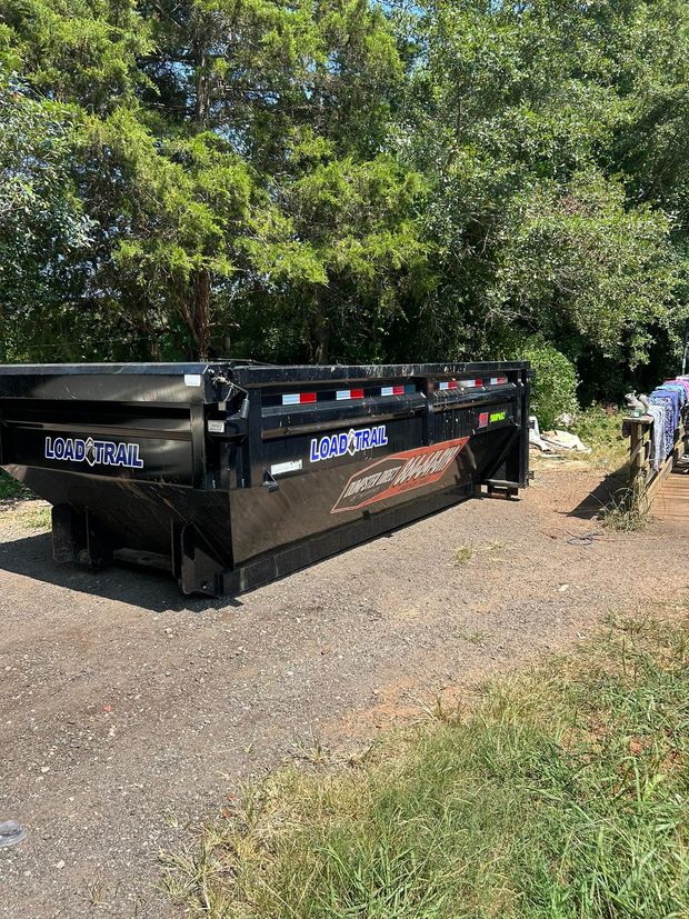 A dumpster is parked on the side of the road next to trees.