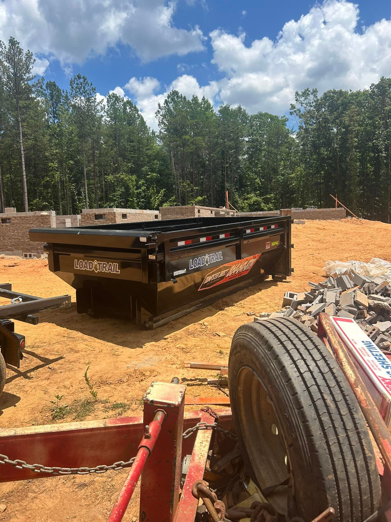 A trailer is sitting on top of a dirt field next to a tire.