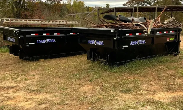 Two dumpsters are sitting on top of a grassy field.