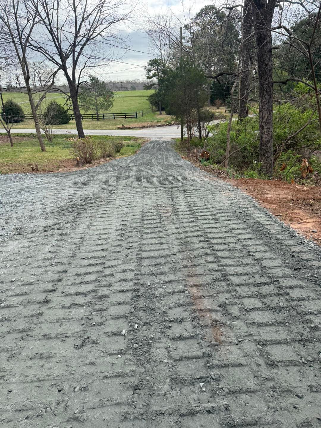 Gravel pathway leads uphill towards a green field and trees on either side. Overcast day.