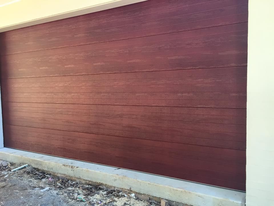 A red garage door is sitting on the side of a building. — P & D Garage Doors in Taree, NSW