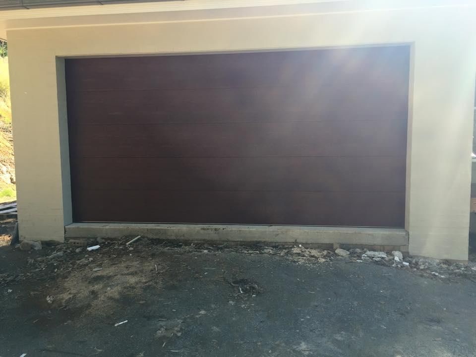 A Brown Garage Door is Sitting Next to a White Wall — P & D Garage Doors in Taree, NSW