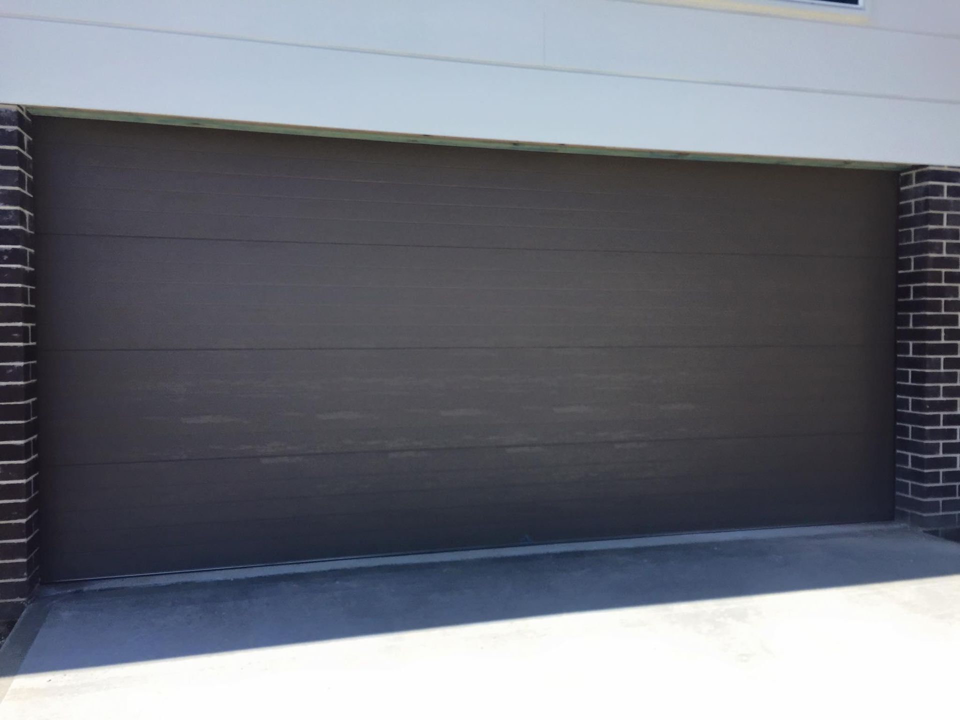 A Brown Garage Door is Sitting Next to a Brick Wall — P & D Garage Doors in Taree, NSW