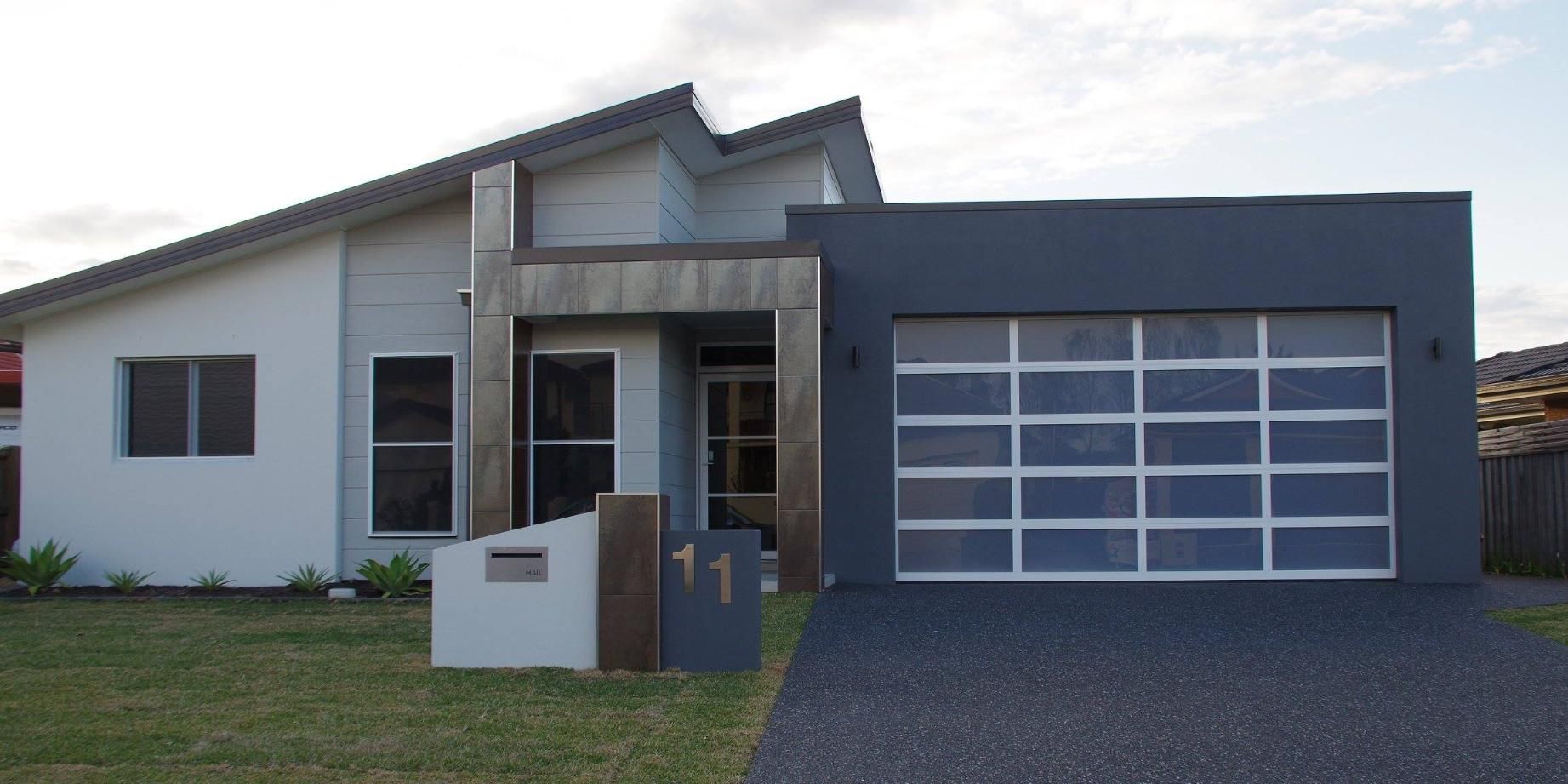 A Large House With a Black Garage Door and a Concrete Driveway — P & D Garage Doors in Port Macquarie, NSW