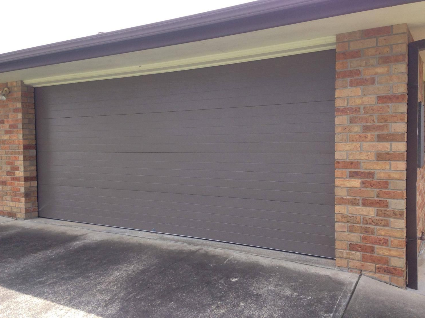 A garage door is sitting in front of a brick building. — P & D Garage Doors in Taree, NSW