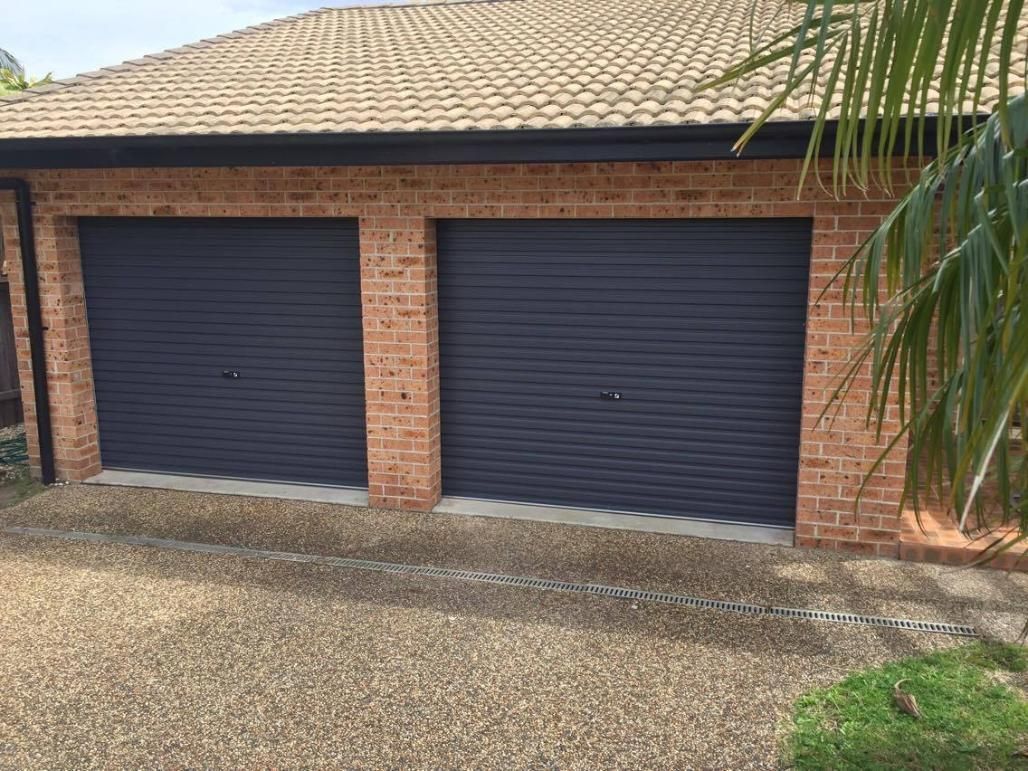 A Brick House With Two Garage Doors and a Palm Tree in Front of It — P & D Garage Doors in Taree, NSW