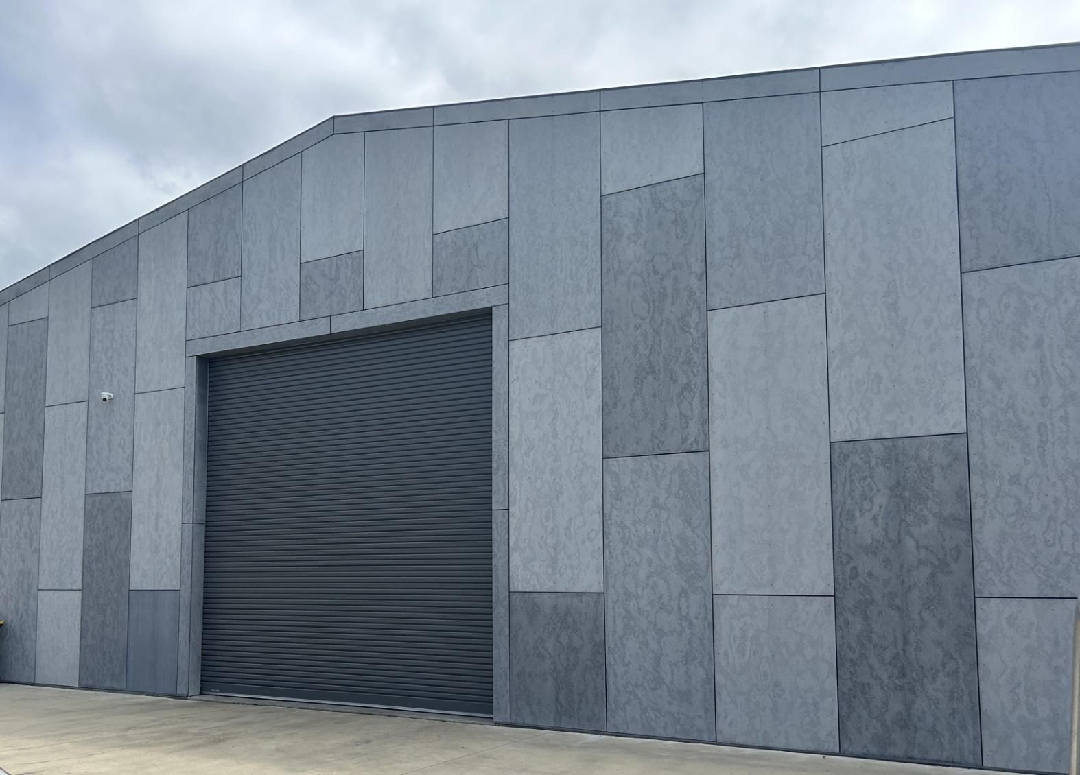 A Large Gray Building With a Black Garage Door — P & D Garage Doors in Taree, NSW