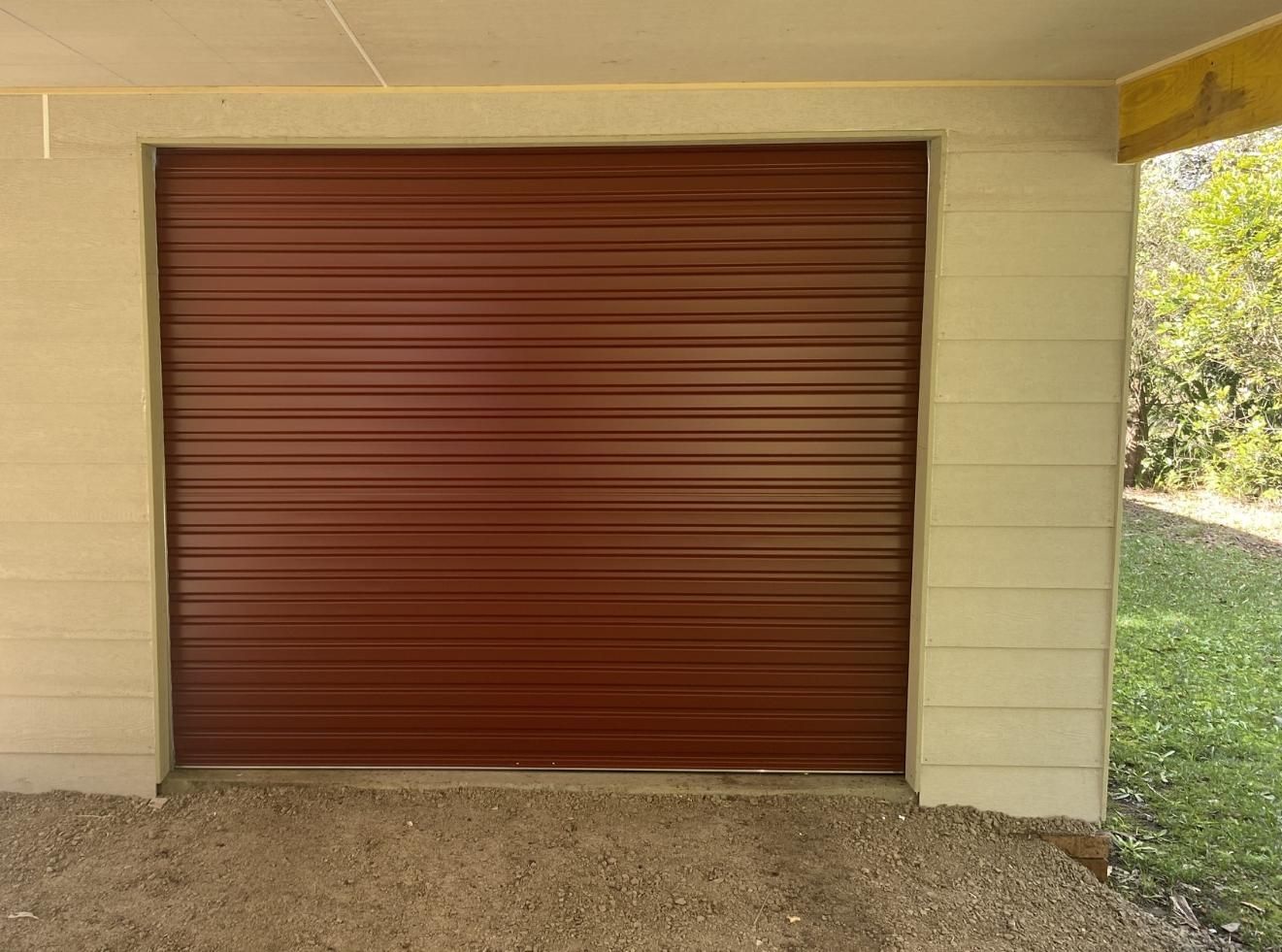 A Brown Garage Door is Sitting Next to a Brick Wall — P & D Garage Doors in Taree, NSW