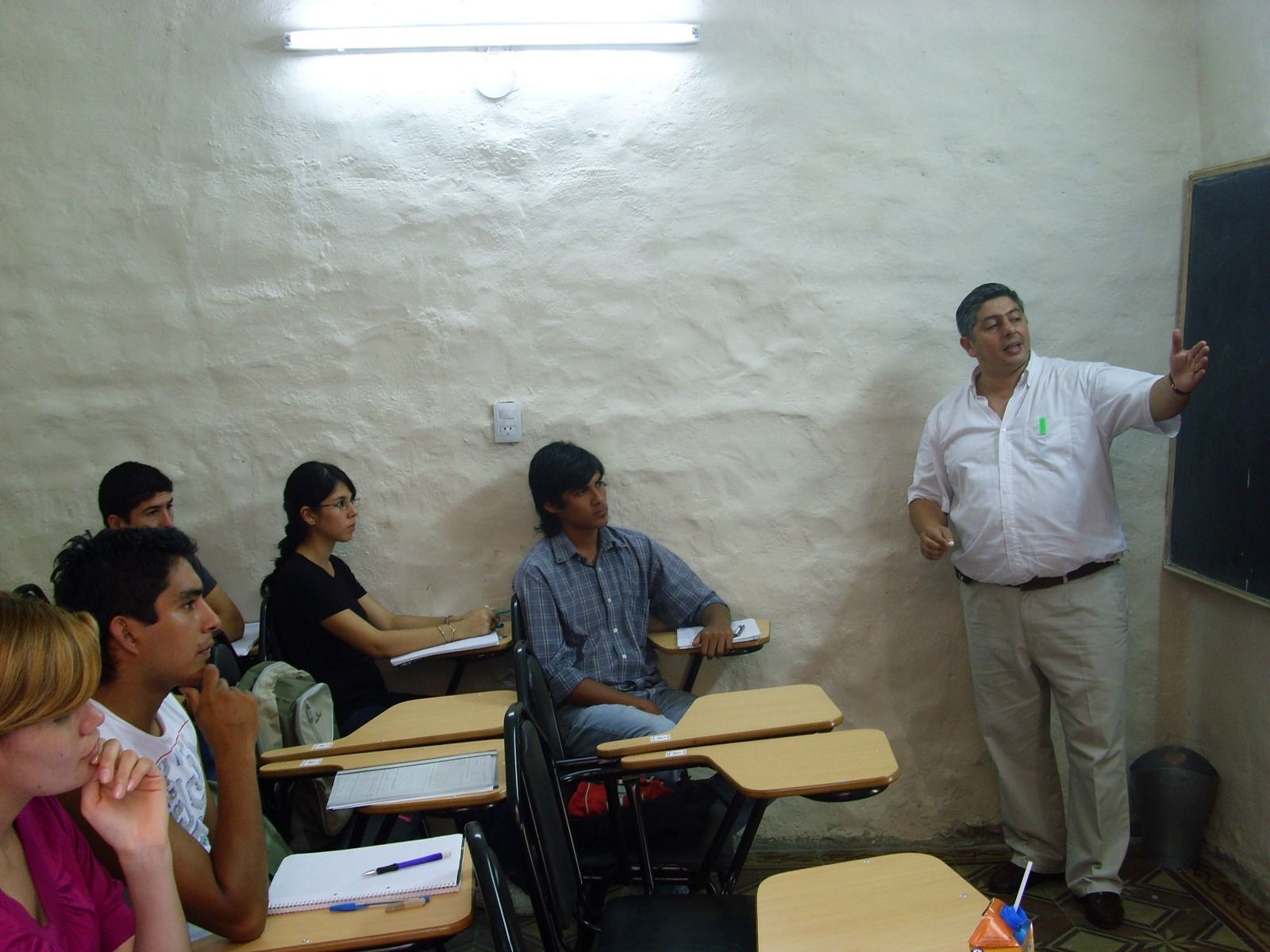 El profesor señala la pizarra en un aula, los alumnos observan.