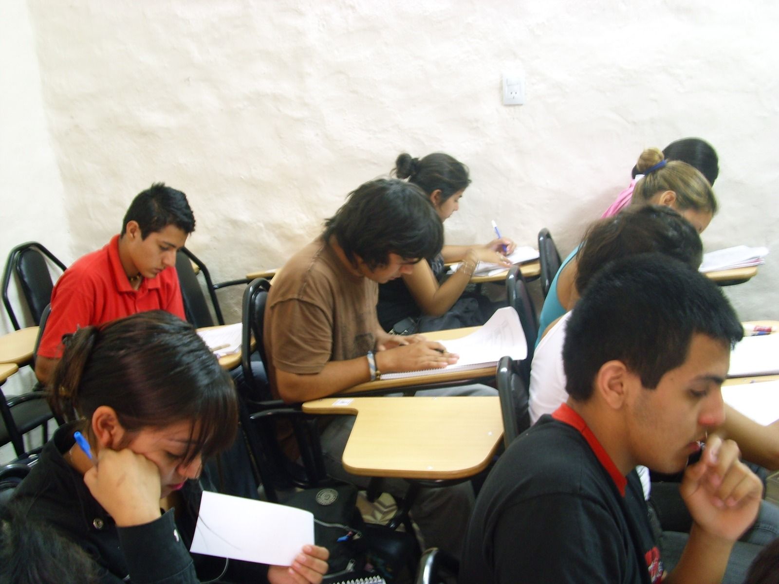 Estudiantes tomando apuntes en un aula, concentrados, en sus pupitres.