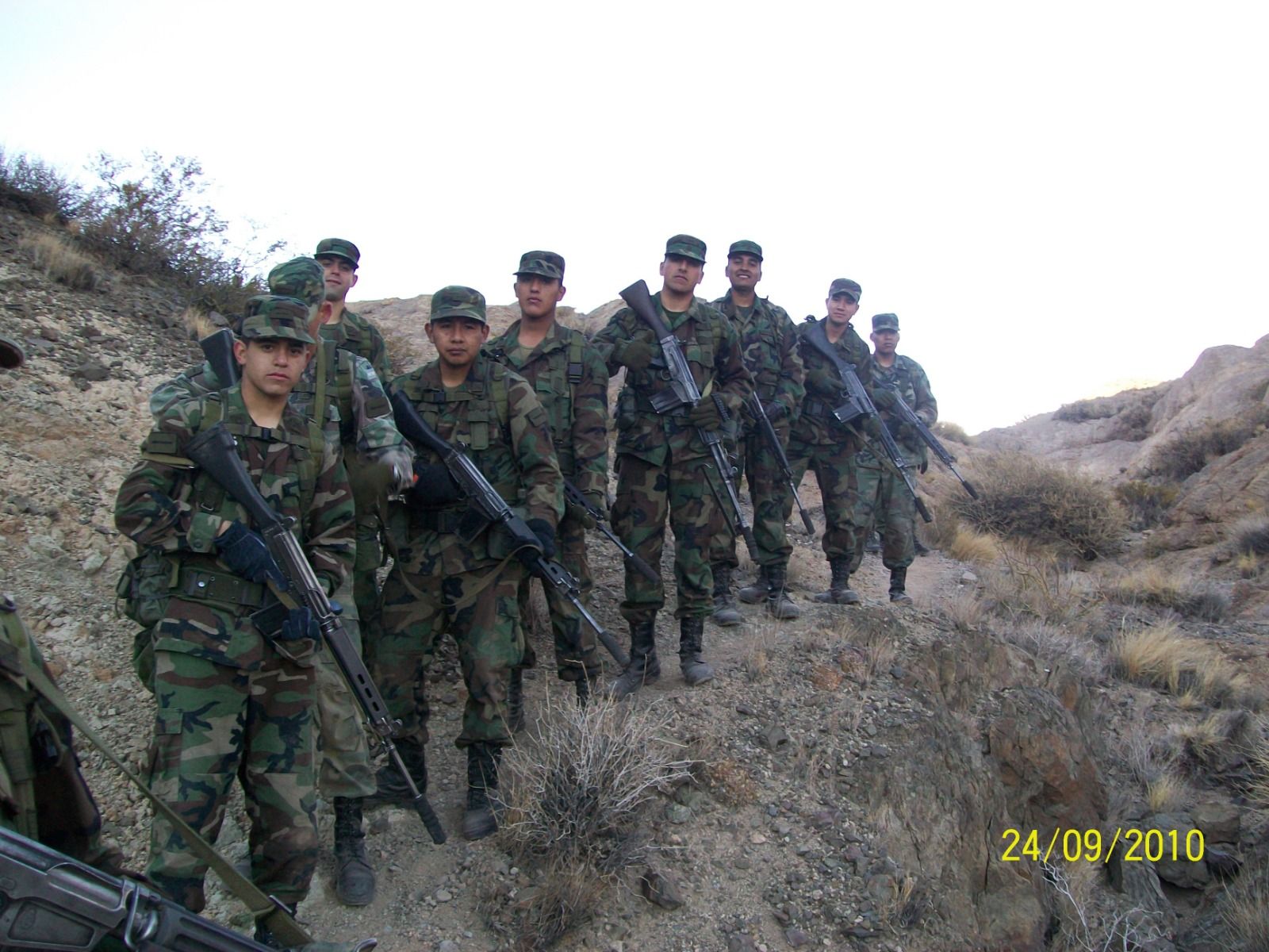 Soldados con uniformes de camuflaje, portando rifles, forman una fila en la ladera de una colina.