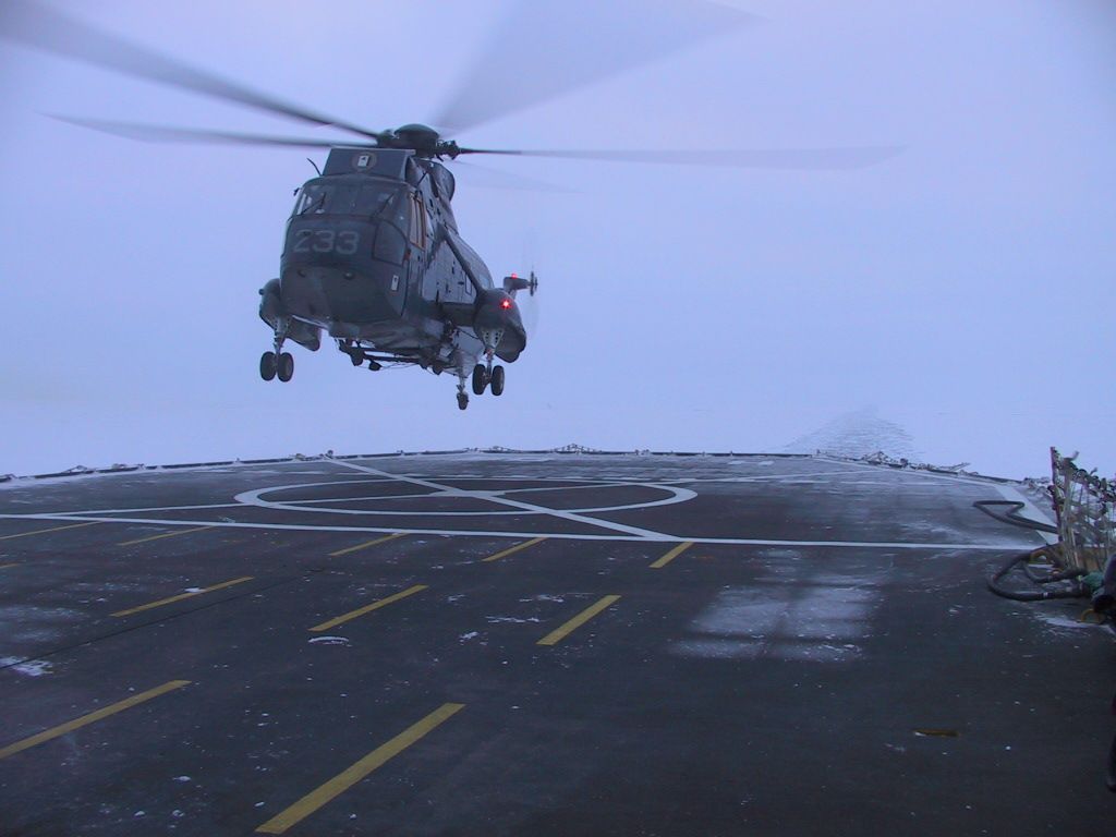 Helicóptero aterrizando en un helipuerto nevado. Cielo gris, helicóptero oscuro, nieve blanca.