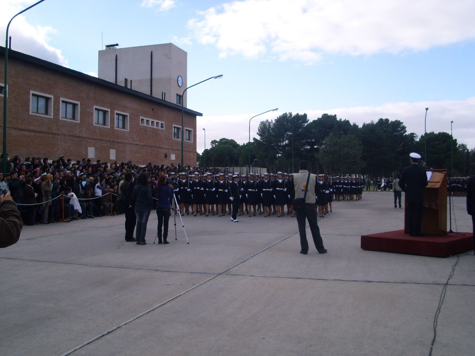 Ceremonia con personal uniformado en posición de firmes frente a un edificio; multitud observando.