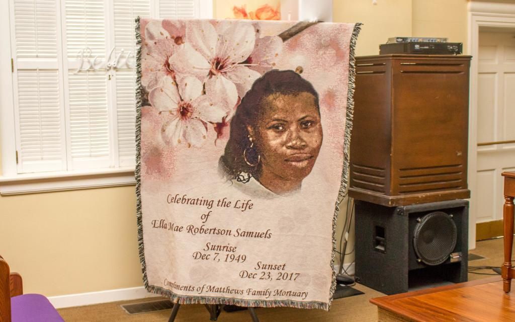 A memorial blanket featuring a woman's portrait, displayed in a room. Includes text and flowers.