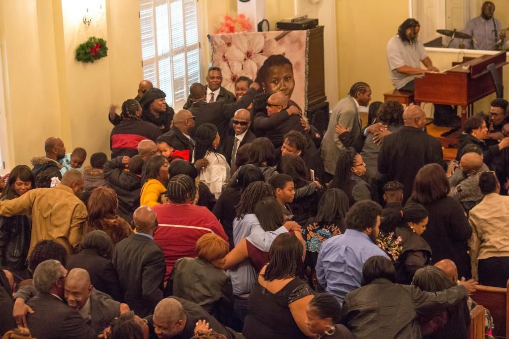 People gathered at a memorial service in a church. A large photo is displayed. A musician plays the organ.
