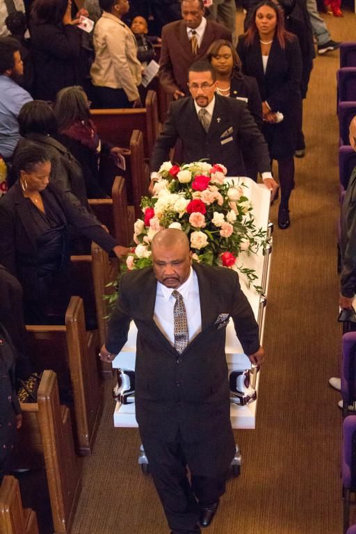 People carry a white coffin with floral arrangement down a church aisle.