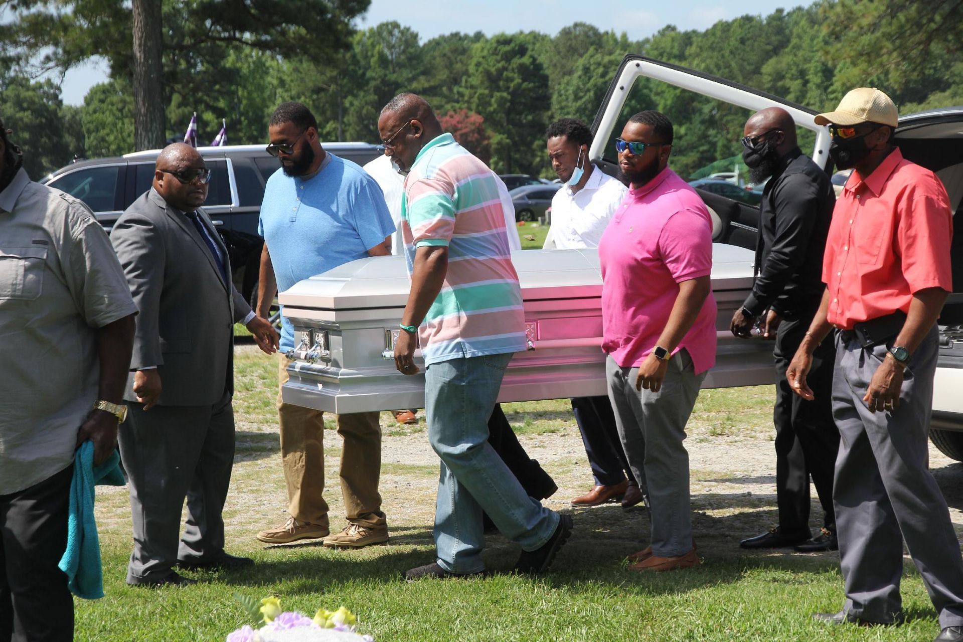 People carry a white coffin outdoors on a sunny day.