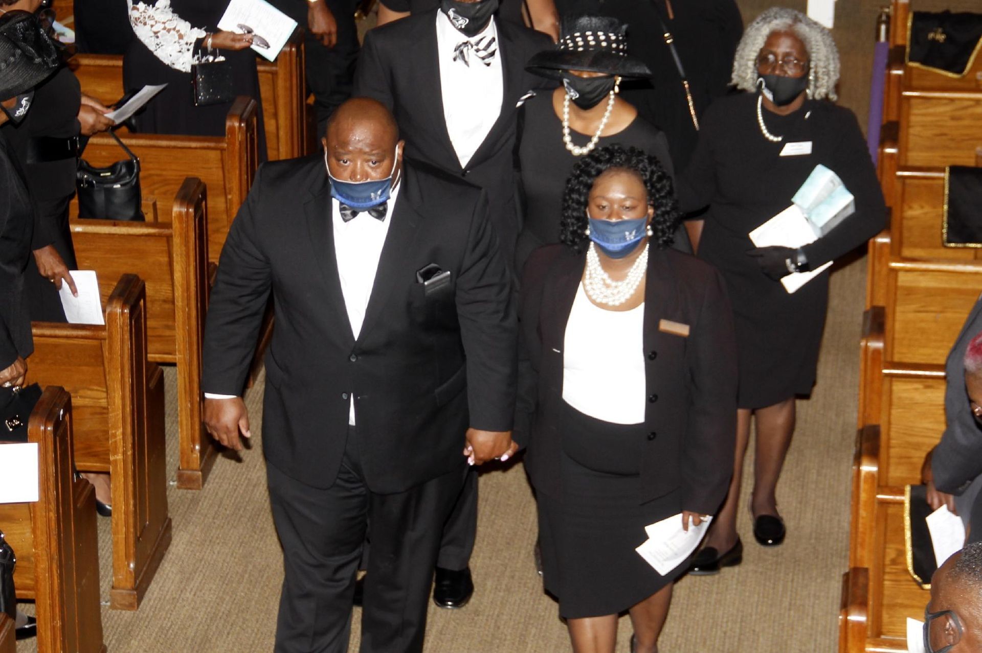 People in formal attire, some wearing masks, walking inside a church.
