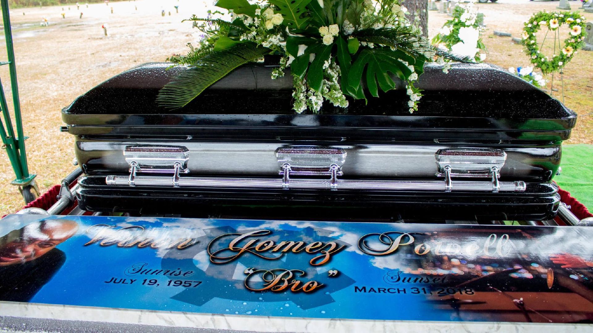 Black casket with floral arrangement at a funeral. Nameplate reads 