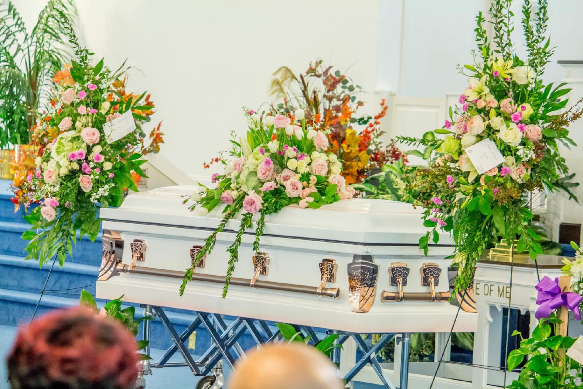 White casket with floral arrangements at a funeral service.