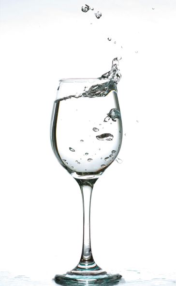A wine glass filled with water, splashing upwards against a white background.