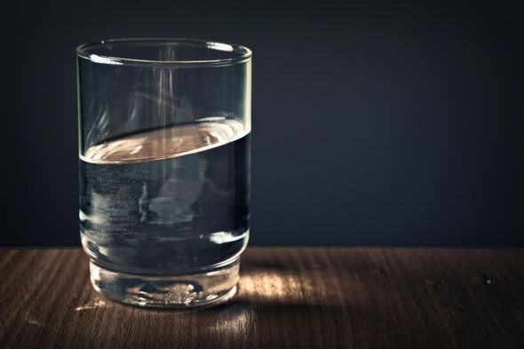 Glass of water, half-full, on a wooden surface against a dark background.