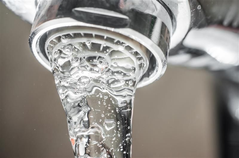 Close-up of water flowing from a chrome faucet with visible bubbles and clear droplets.