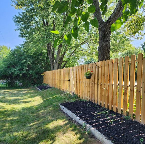 A wooden residential picket fence surrounds a lush green yard