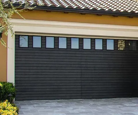 Dark gray horizontal-paneled garage door with rectangular windows above, set in a stone driveway.